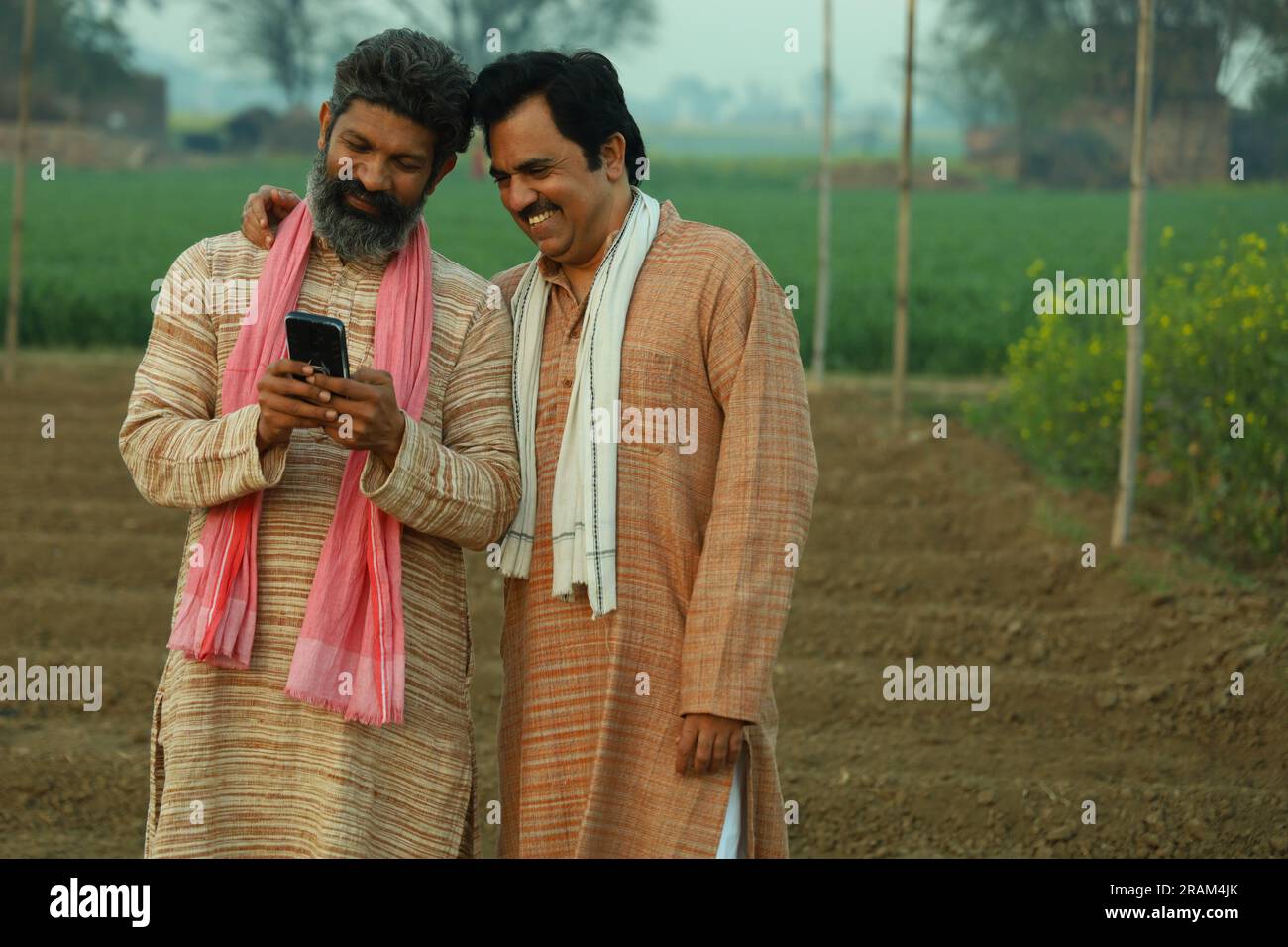 Beautiful composition of two Indian farmers standing in the field . Agriculture concept portraying the farmers at work looking into the smartphone. Stock Photo