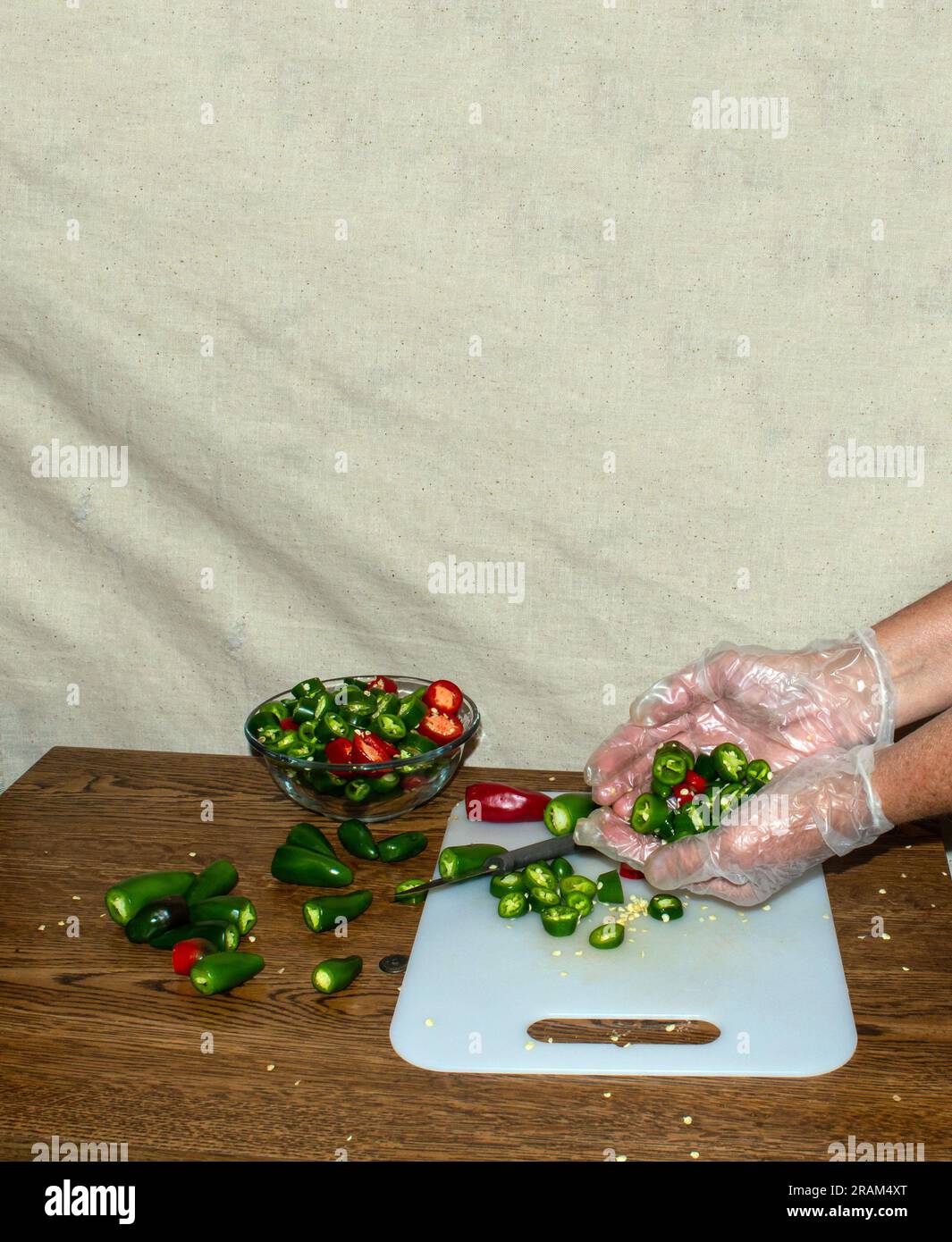 The jalapeno peppers have been washed and are being sliced. The kitchen workers wears gloves and holds a handful of the sliced vegetable. Stock Photo