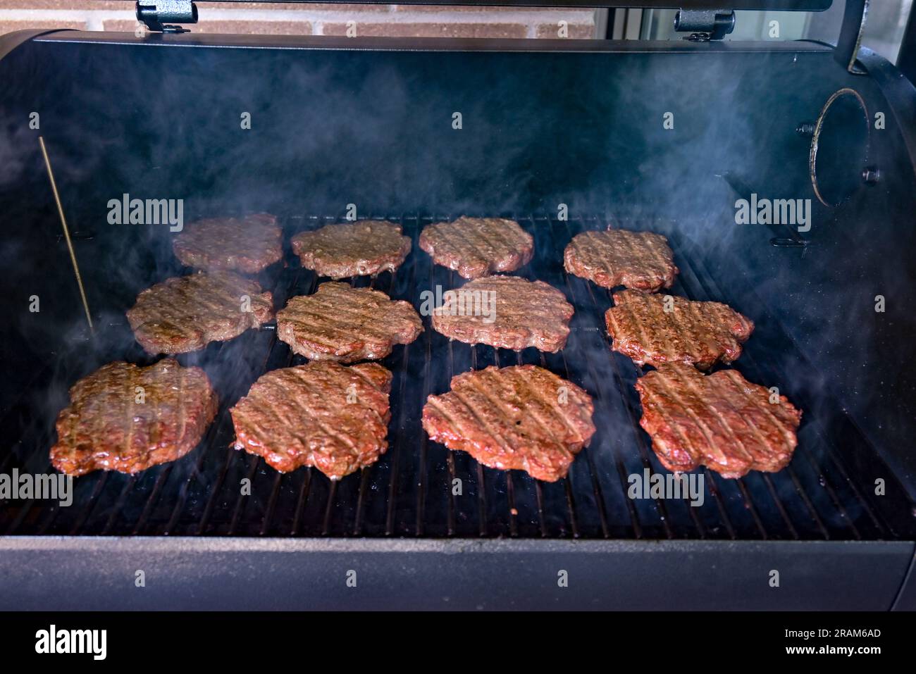 Burger patties on top of the grill being cooked, with smoke in the back