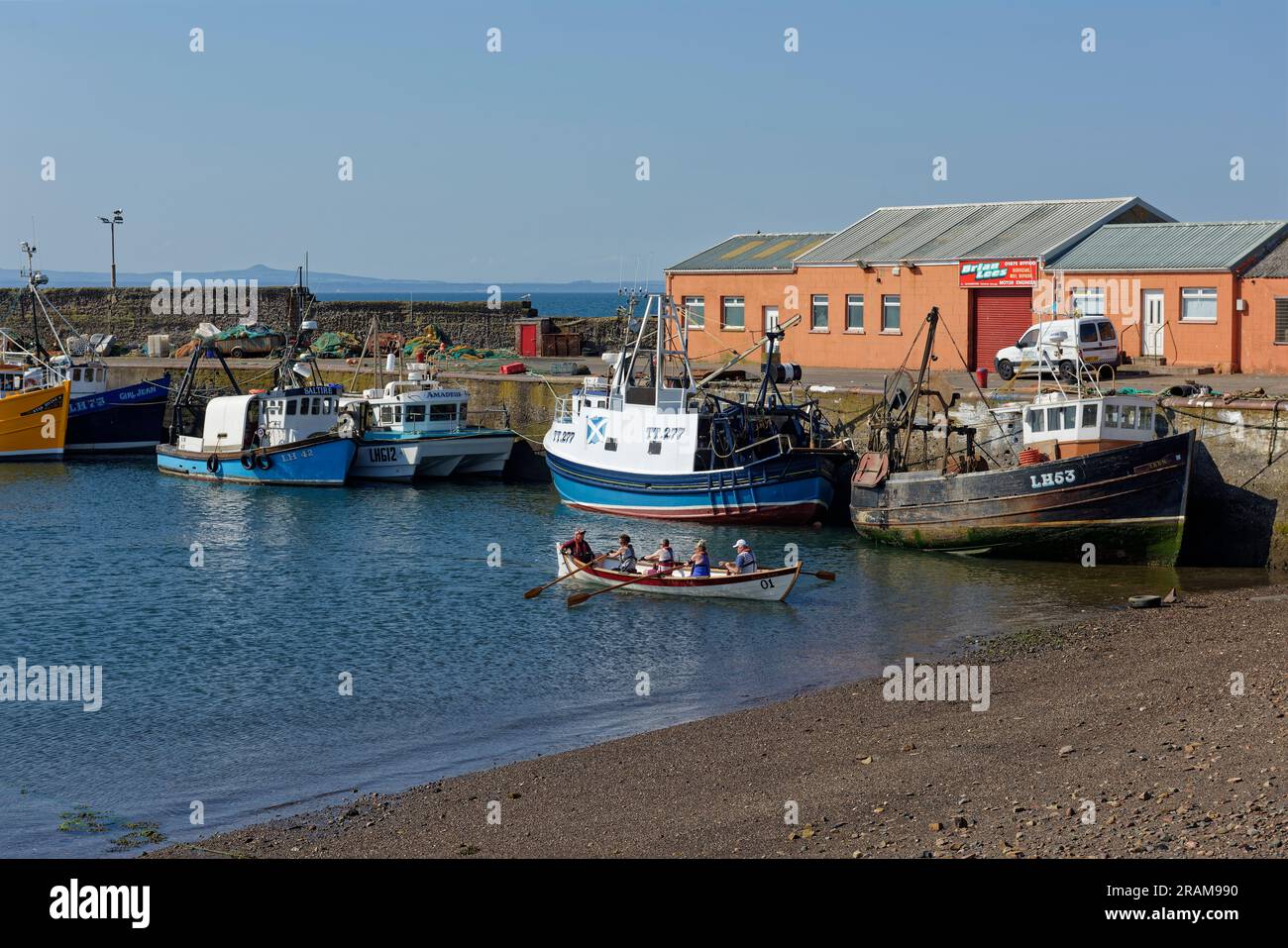 Five People in a wooden Rowing boat with a white Hull coming in to the shallow beach at Port Seton Harbour near to Edinburgh. Stock Photo