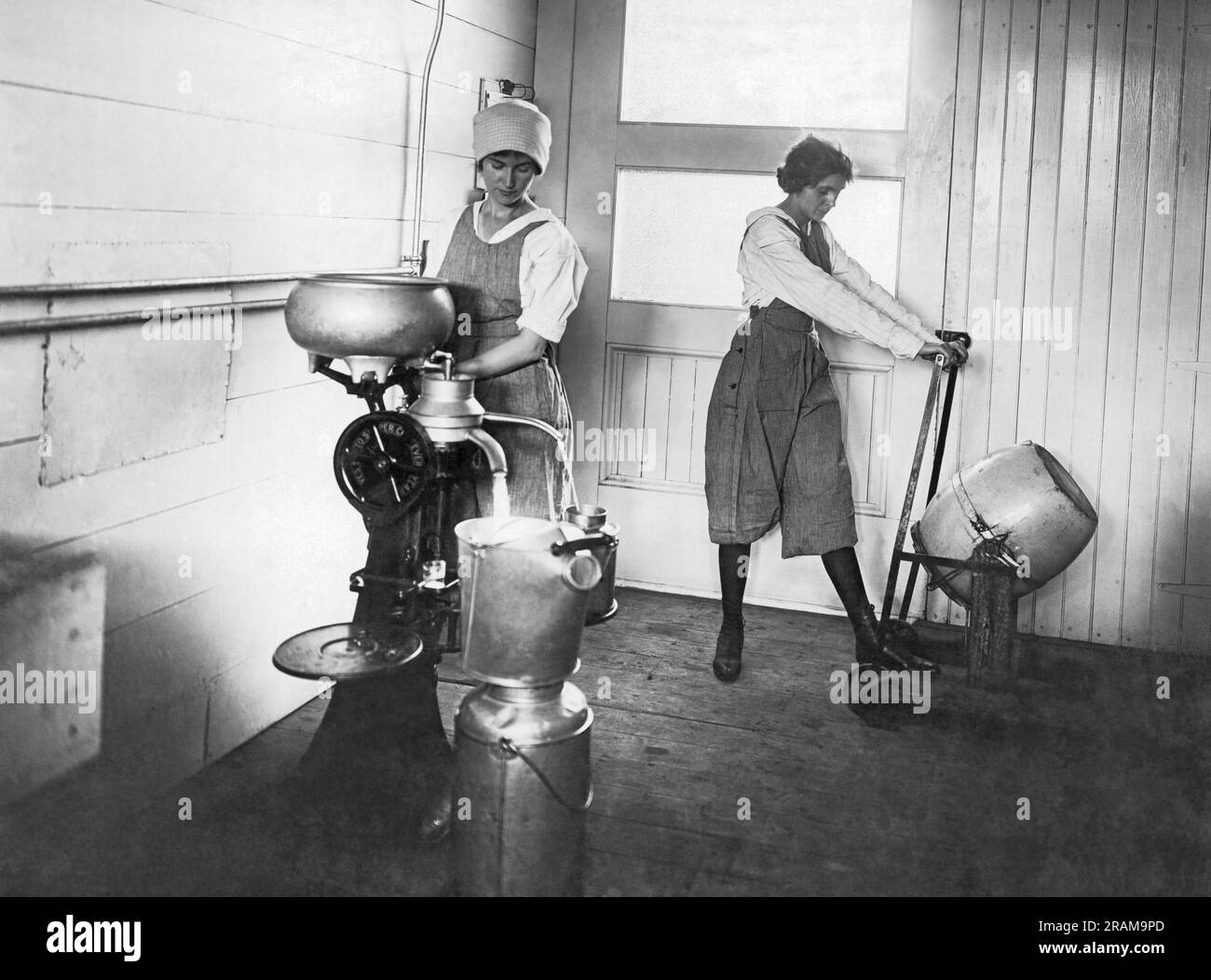 United States:   c. 1920 Two women working in a dairy with one separating the cream from the milk and the other is churning butter. Stock Photo