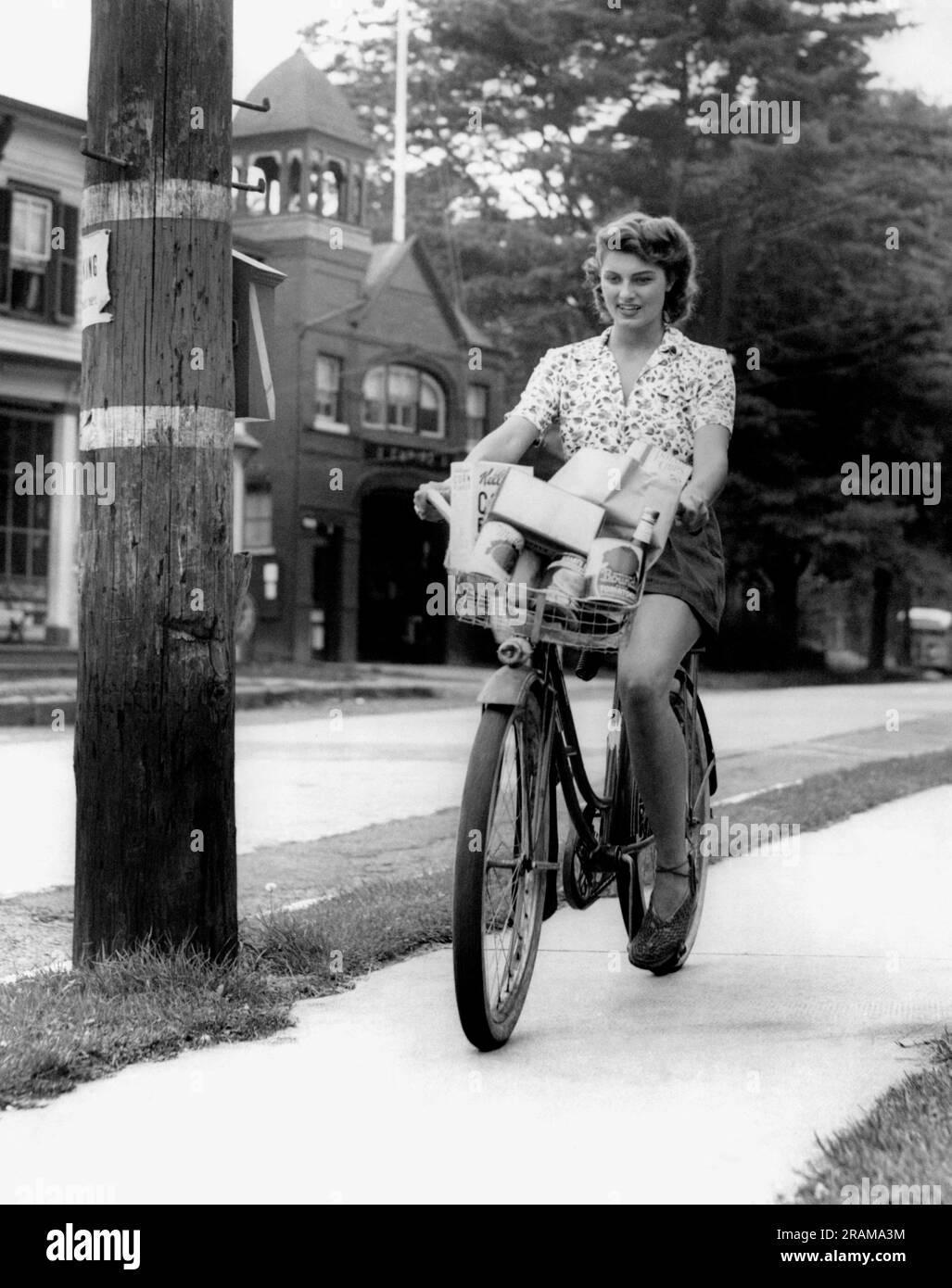 United States c. 1946 A young woman rides her bike with a basket full