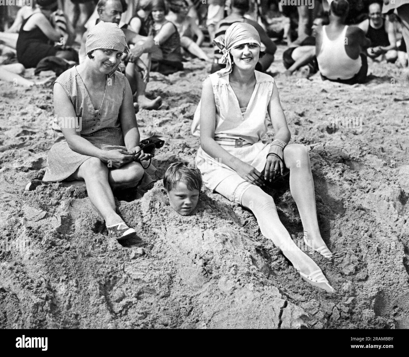 Miami Beach, Florida:  February, 1925 A young boy has been buried up to his neck in sand and is now happily watched over by two women. Stock Photo