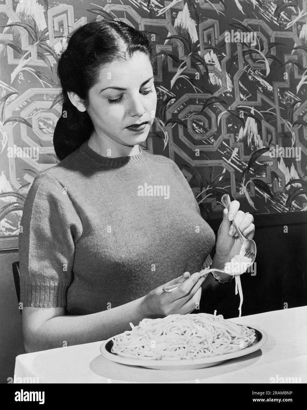 United States:  June, 1948 An Instructer at the Foods Institute demonstrates the correct way eat spaghetti using a fork and soup spoon. Stock Photo