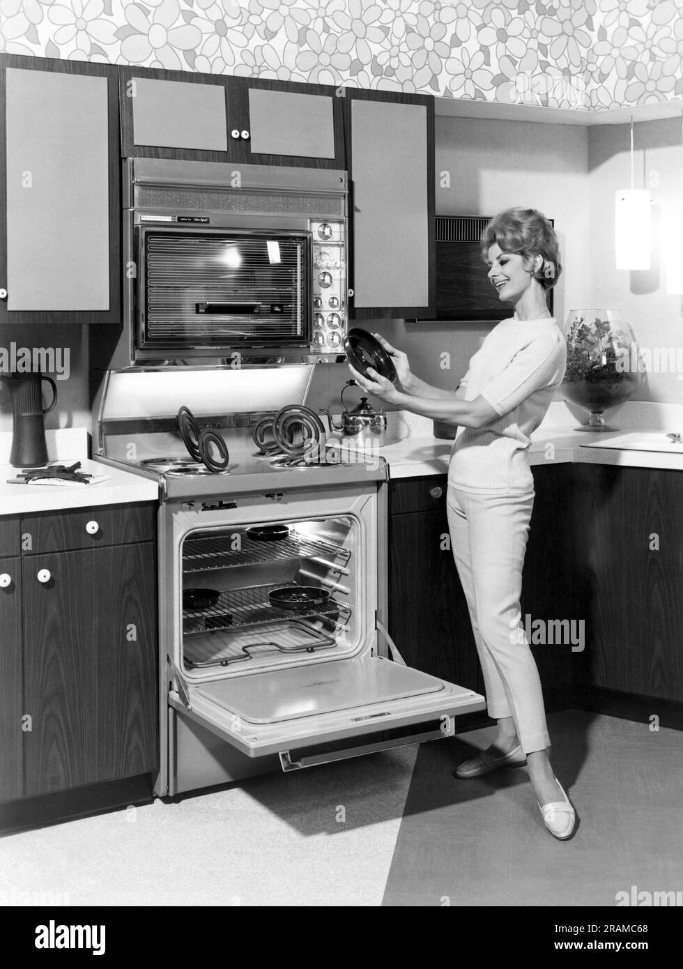 United States:  1967 A young woman looks happily upon her stove top parts that have been cleaned in the self cleaning feature of her oven. Stock Photo