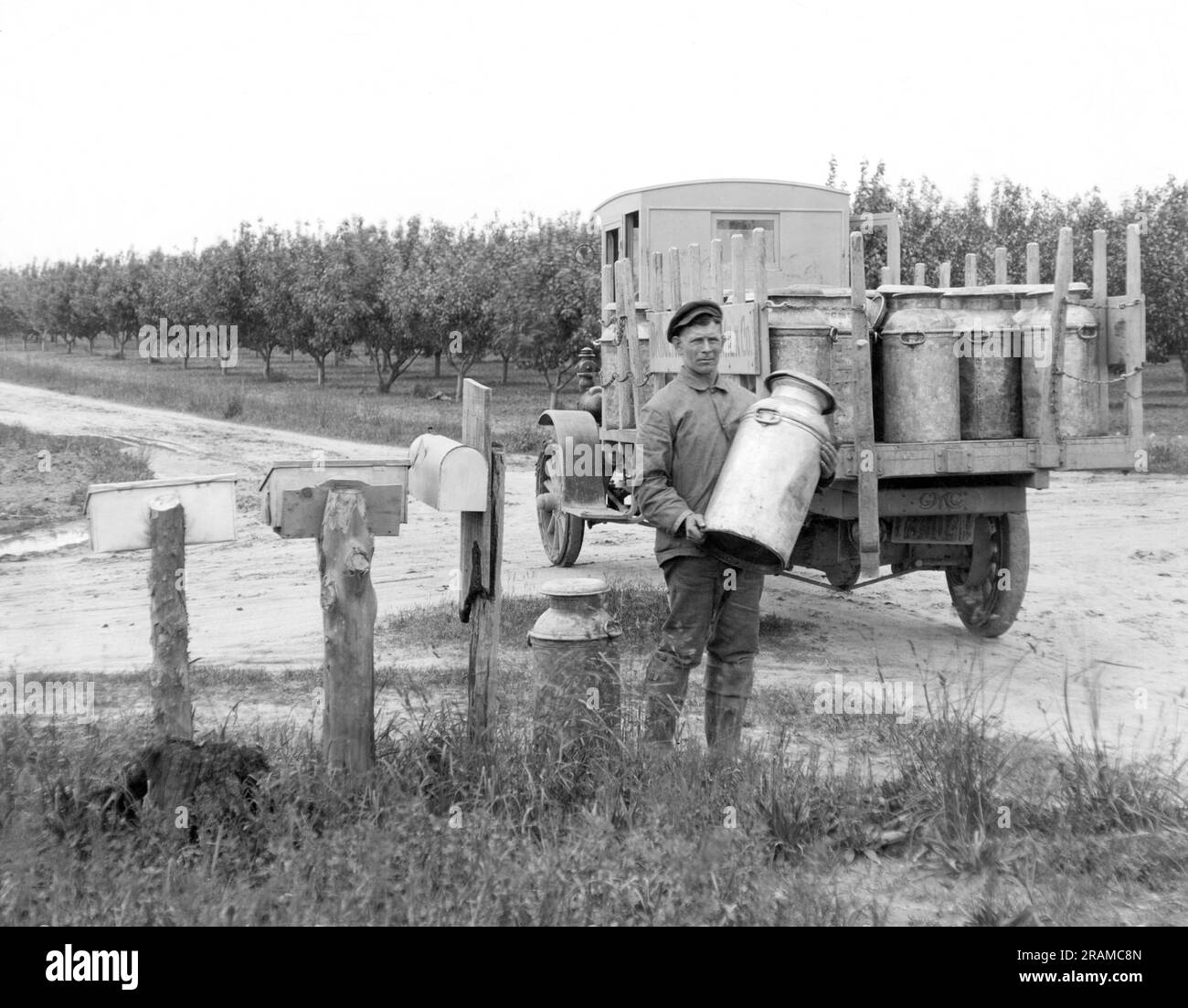United States:   c. 1920 A milk company employee picking up cans of milk from local dairy farmers. Stock Photo