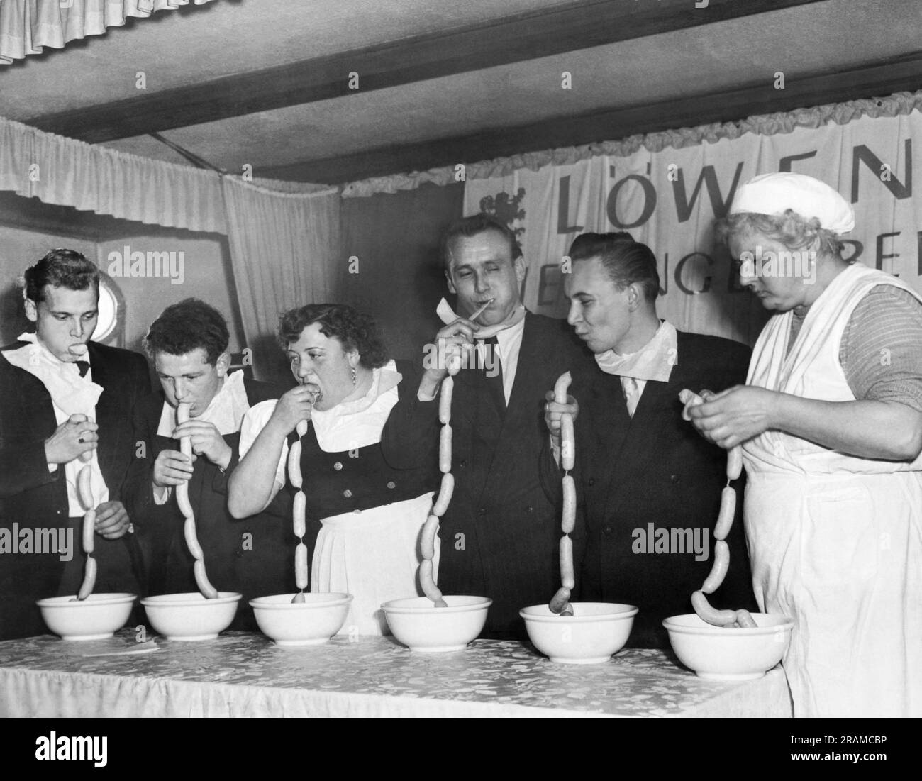 Munich, Germany:  November 19, 1952 Contestants at a Bavarian white suasage eating contest gobble away at chains of the delicacies at a Munich beer hall. The winner, Rudi Sachs, second from left, practically inhaled a chain of 15 sausages in 1 minute and 45 seconds. Stock Photo