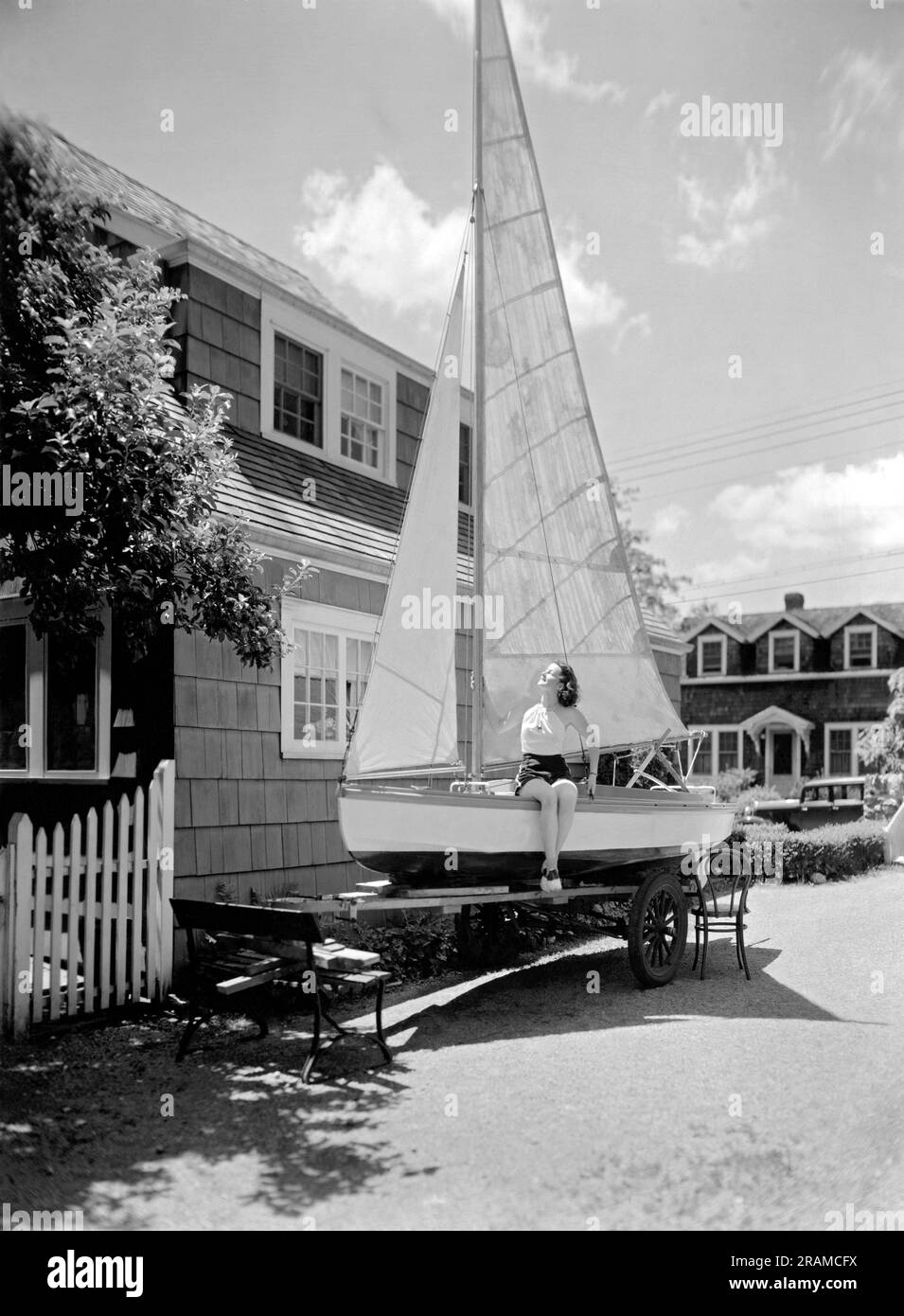 United States:   c. 1933. A young woman catches some rays from the sun on the deck of a sailboat that is on a trailer in the driveway Stock Photo