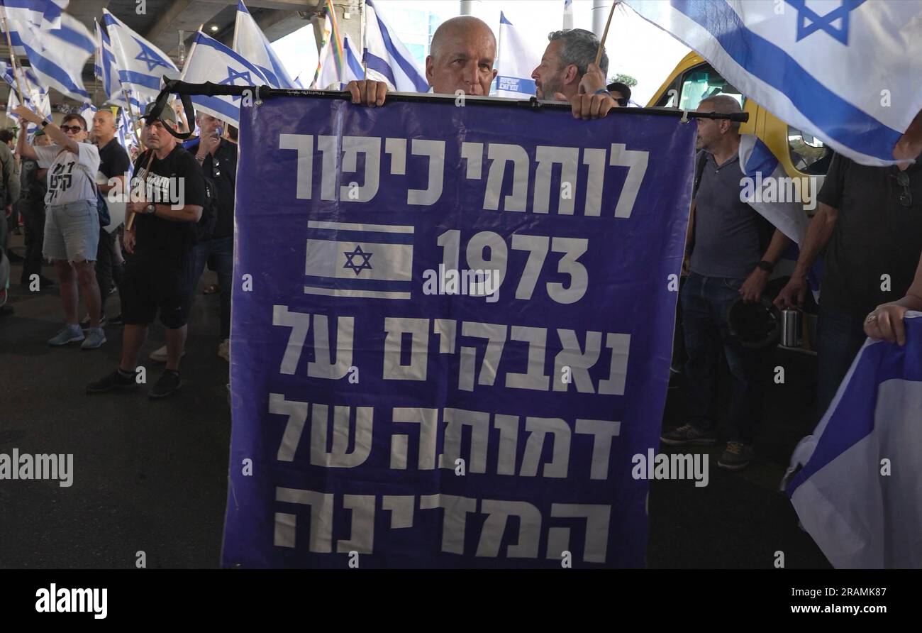 A protester holds a sign which reads 'The veterans of the 1973 Yom Kippur War are fighting for the state's image' as anti-government protestors gather outside Israel's main international airport during a protest against PM Benjamin Netanyahu and Israel's hard-right government judicial system plan that aims to weaken the country's Supreme Court, at Ben Gurion Airport near Tel Aviv on July 3, 2023 in Lod, Israel. Stock Photo