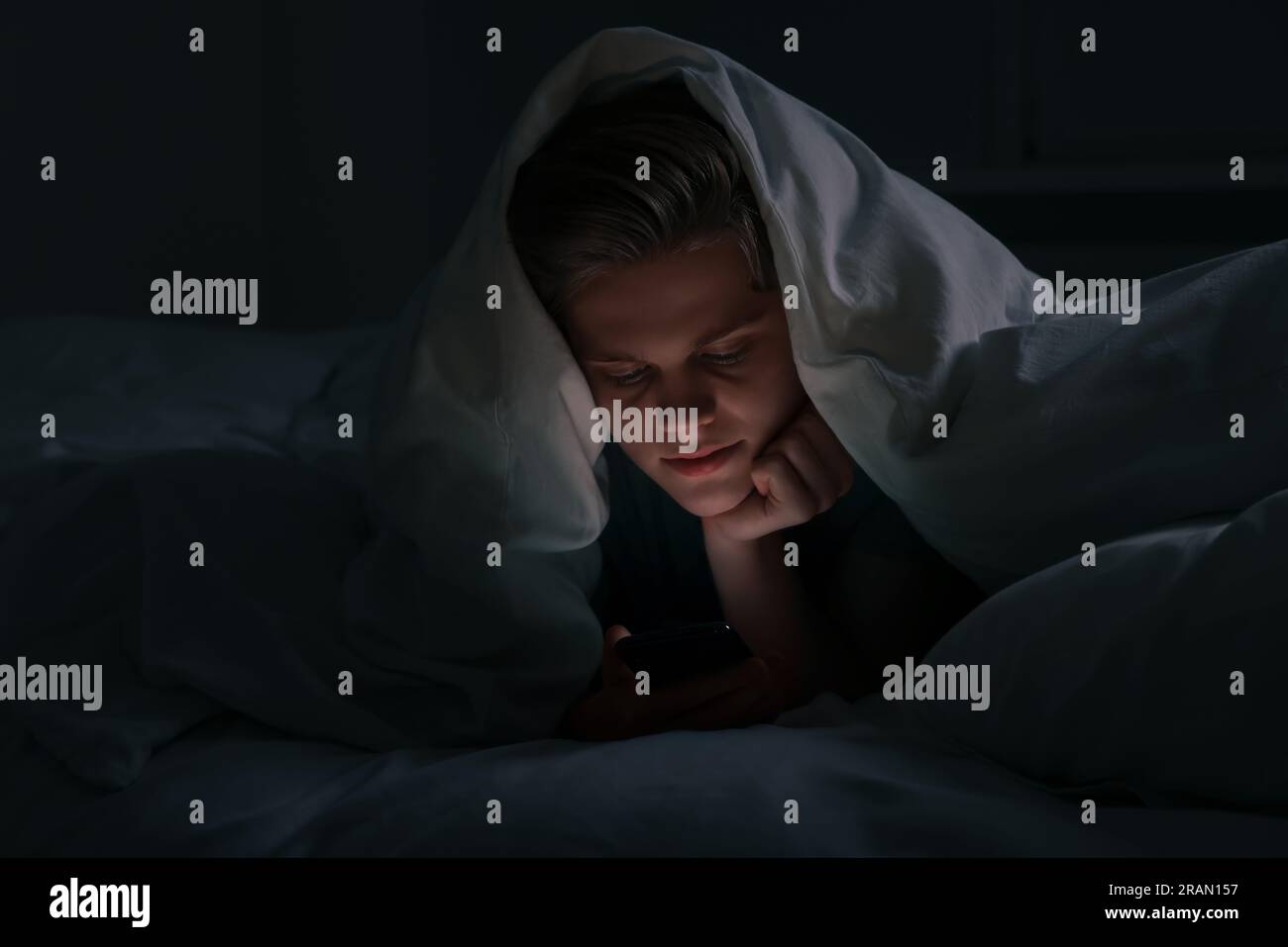 Teenage boy using smartphone under blanket on bed at night. Internet addiction Stock Photo