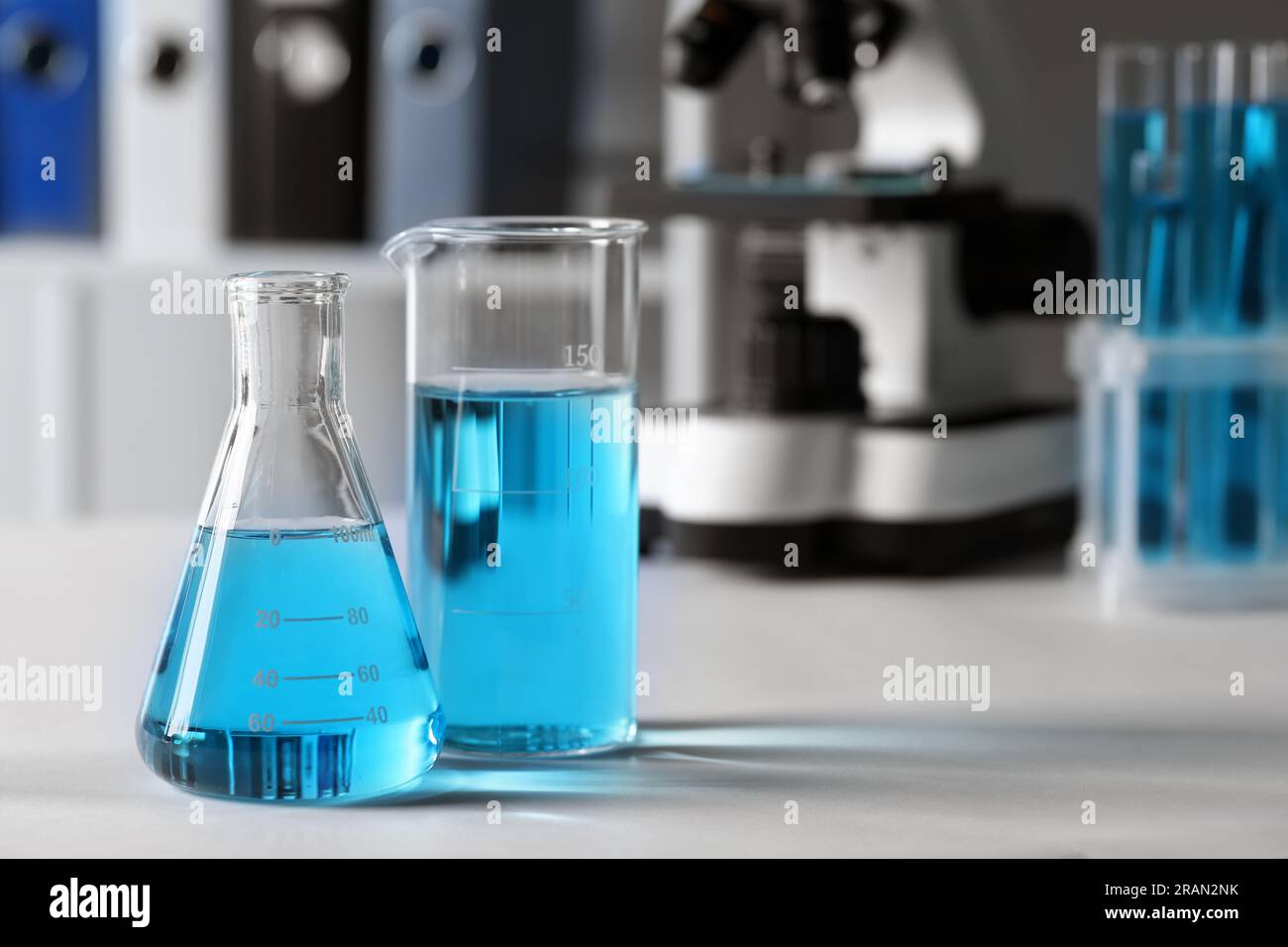Different laboratory glassware with light blue liquid on table. Space ...