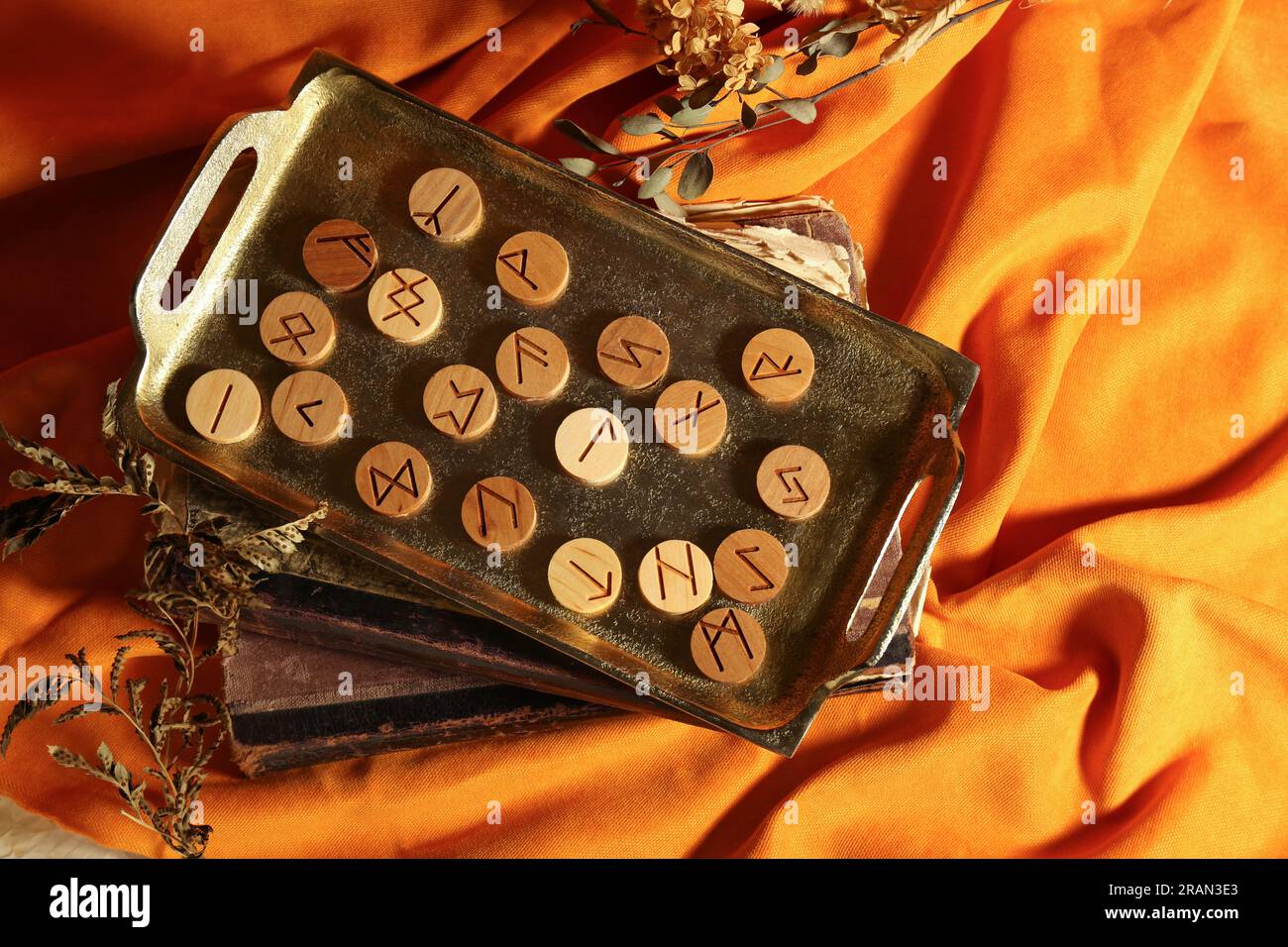 Tray with wooden runes, dried plants and old books on orange fabric ...