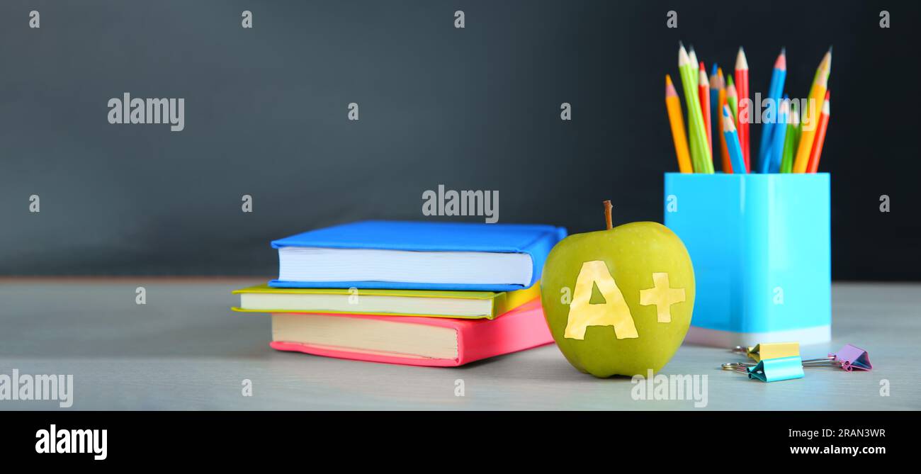 Apple with carved letter A and plus symbol as grade. School stationery on white table in classroom. Banner design with space for text Stock Photo
