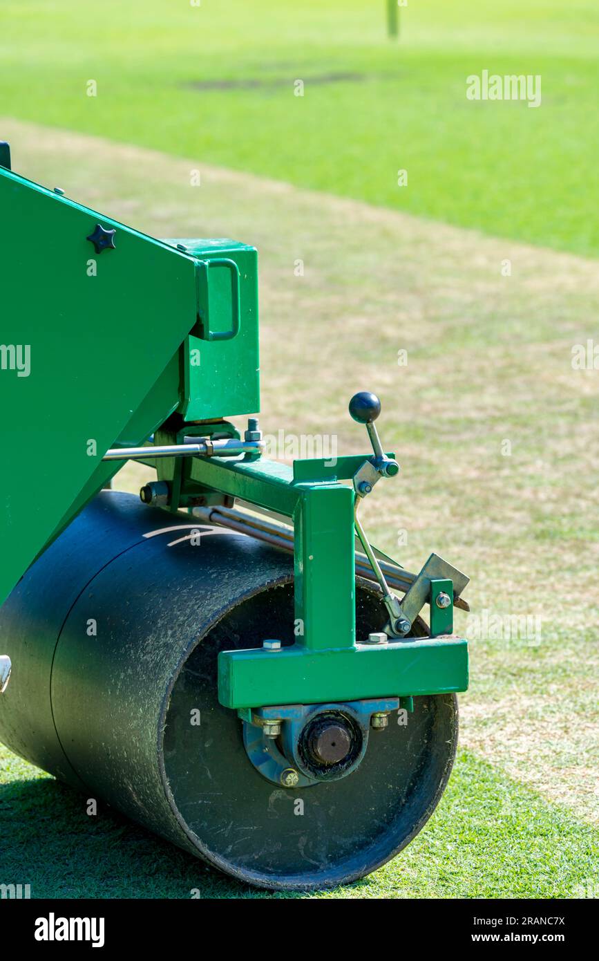 A mechanised heavy pitch roller parked beside a cricket pitch on a