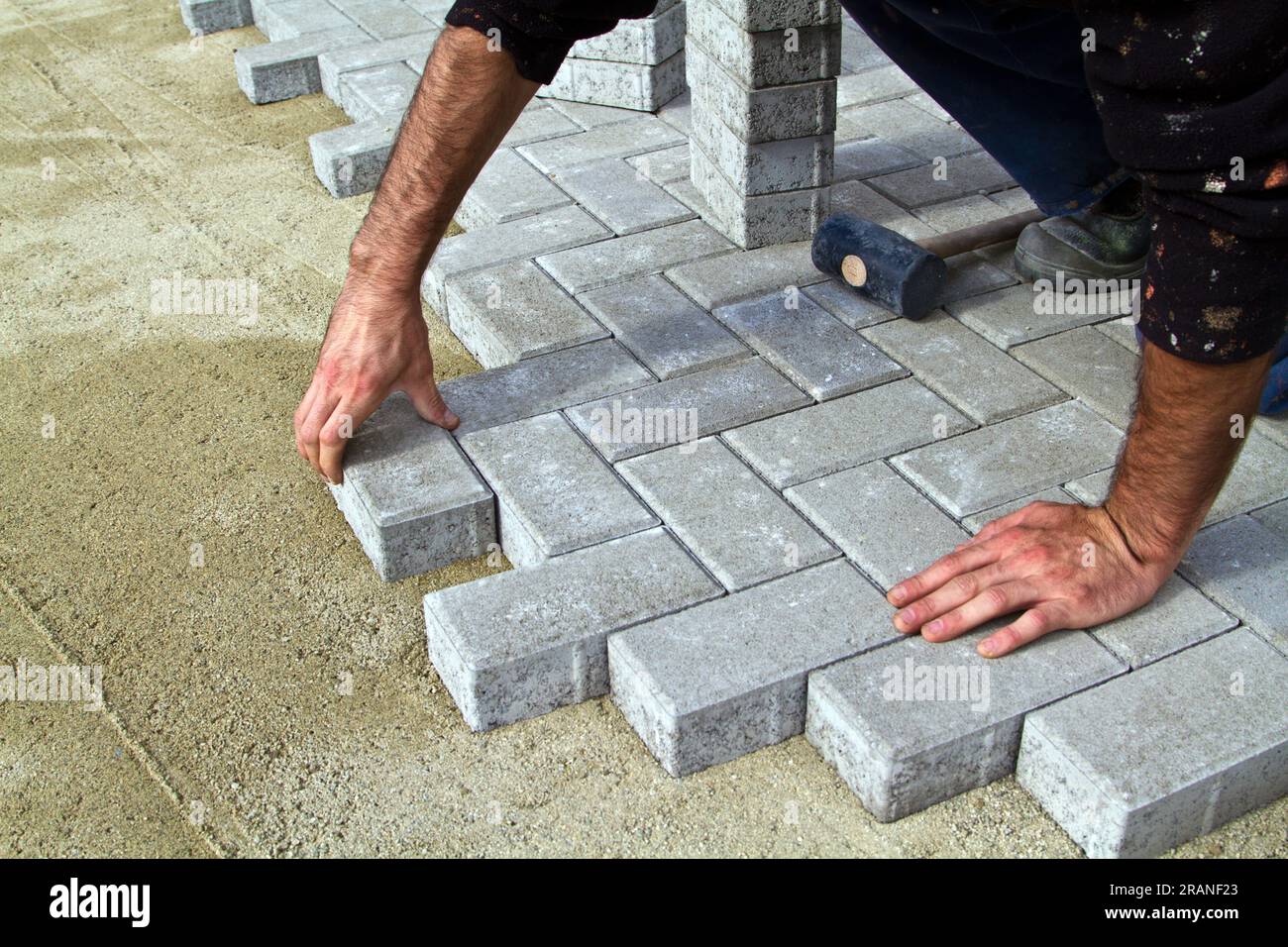 A worker lays concrete paving blocks to build a terrace using a hammer