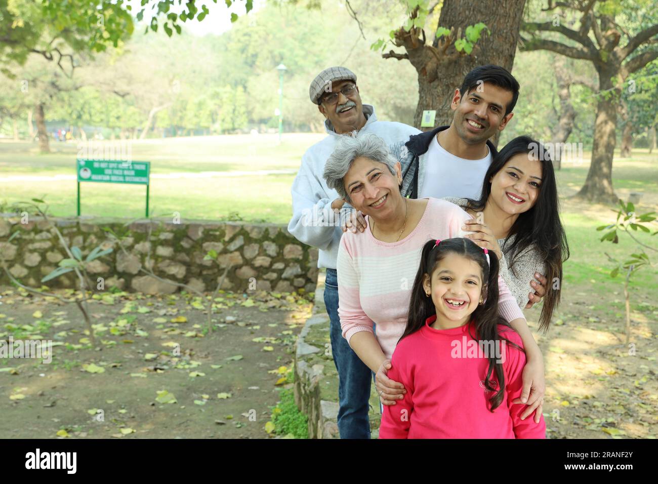 Grandparents enjoying with grand daughter in park, surrounded with greenery and serenity. They are having joyful and cheerful time together in greens. Stock Photo