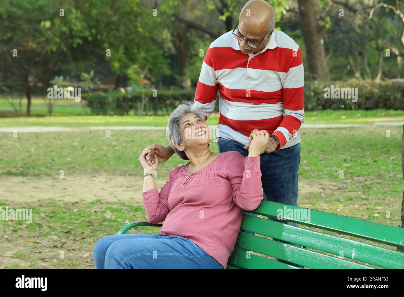Old age couple sitting on the bench in a lush green serene environment having a good time together. They are happily enjoying their time. Stock Photo