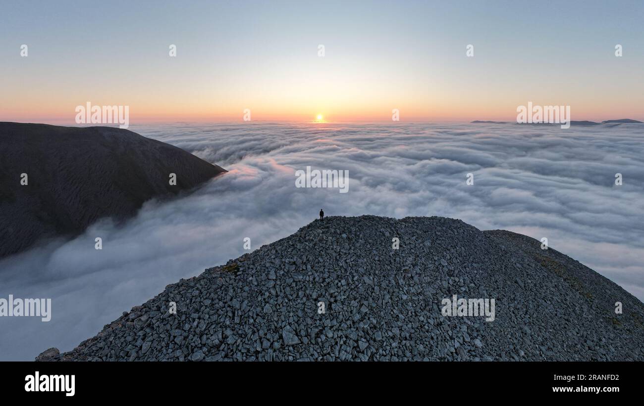 Hiker looking at the sunrise on top the clouds on a Scottish mountain, witnessing a cloud inversion over An Teallach Stock Photo