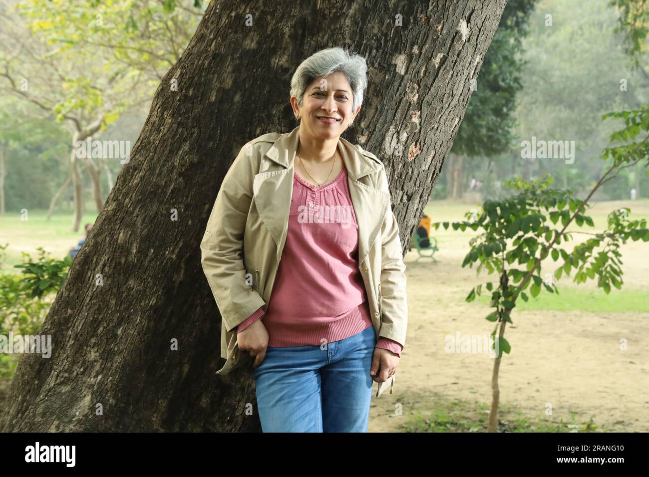 Portrait of mid aged grey hair woman standing under tree in park surrounded with serene environment and clean air. Stock Photo