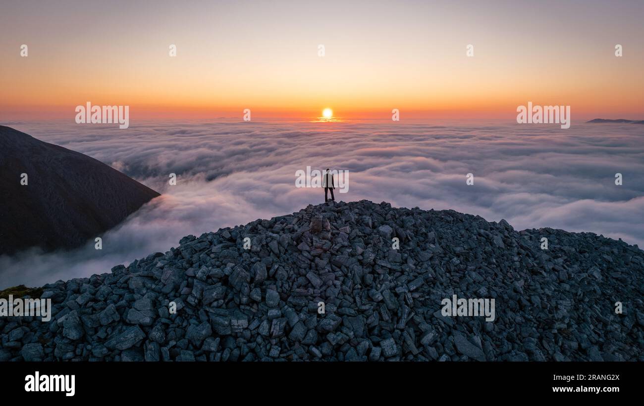 Hiker looking at the sunrise on top the clouds on a Scottish mountain, witnessing a cloud inversion over An Teallach Stock Photo