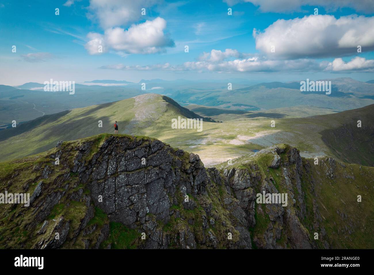 An aerial panorama capturing a hiker standing on a mountain ridge in the Scottish wilderness on a summers day Stock Photo