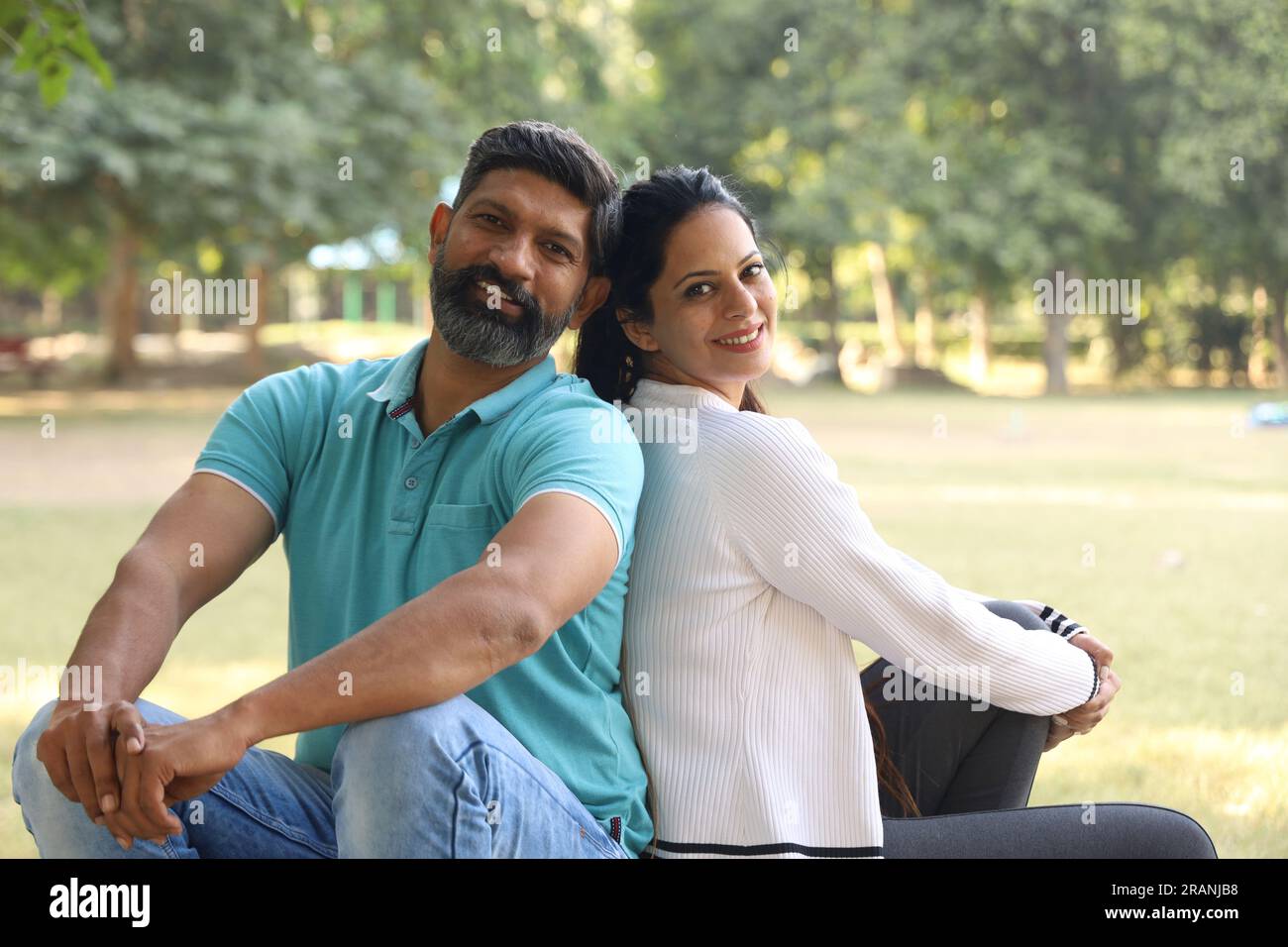 Portrait of a happy Indian couple sitting on the pedestal in the park ...