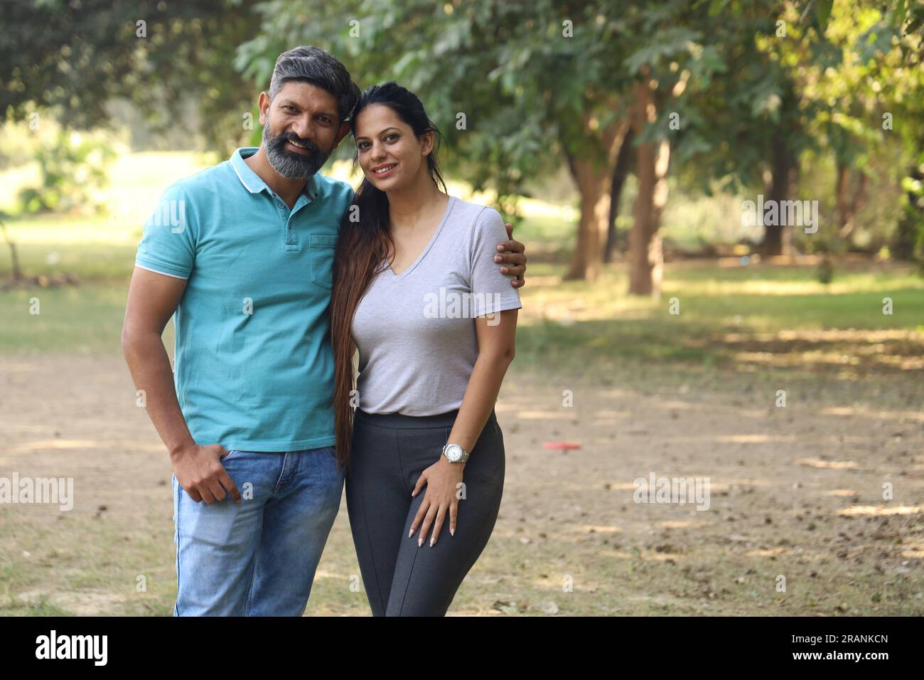 Portrait of a happy Indian couple sitting on the pedestal in the park ...