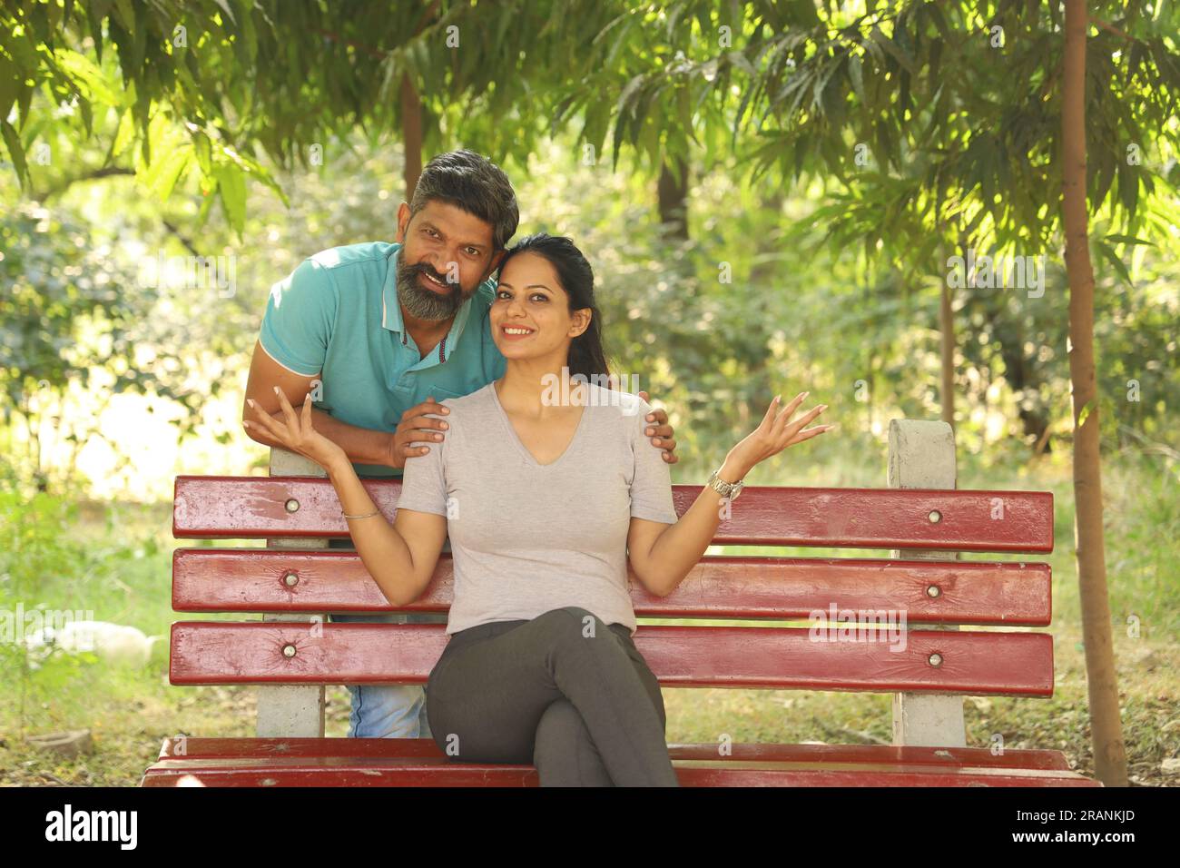 Portrait of a happy Indian couple sitting on the bench in the park ...