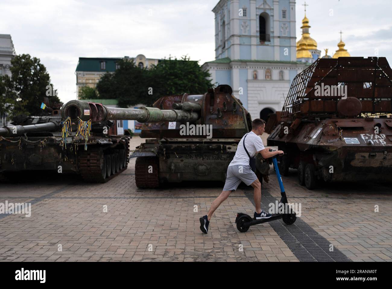 Man Rides Tanks A man rides an electric scooter past destroyed Russian tanks on display ...