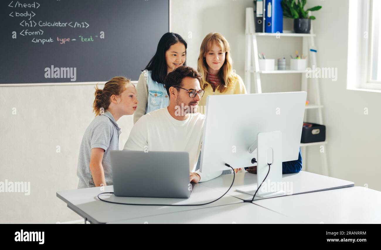 Primary school teacher giving a coding lesson to a group of kids in a ...