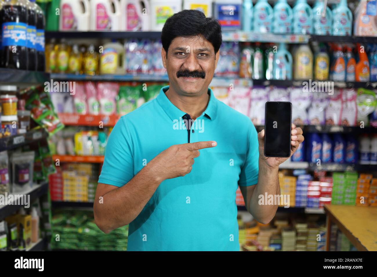 Smiling mid aged man purchasing in a grocery store pointing towards the mobile app. Buying grocery in supermarket pointing towards the mobile app. Stock Photo