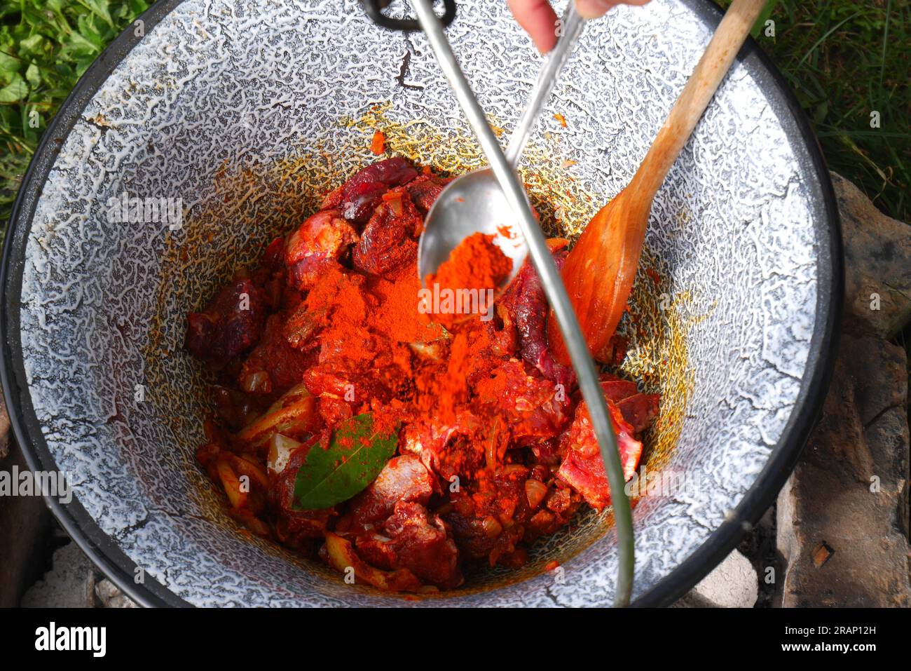 Making Hungarian Gulyas in a cauldron, Bogracs, , in the garden, adding the paprika powder Stock Photo