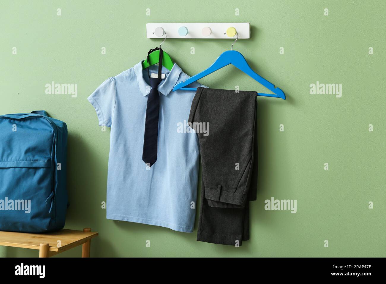 Stylish school uniform hanging on rack with backpack against green wall