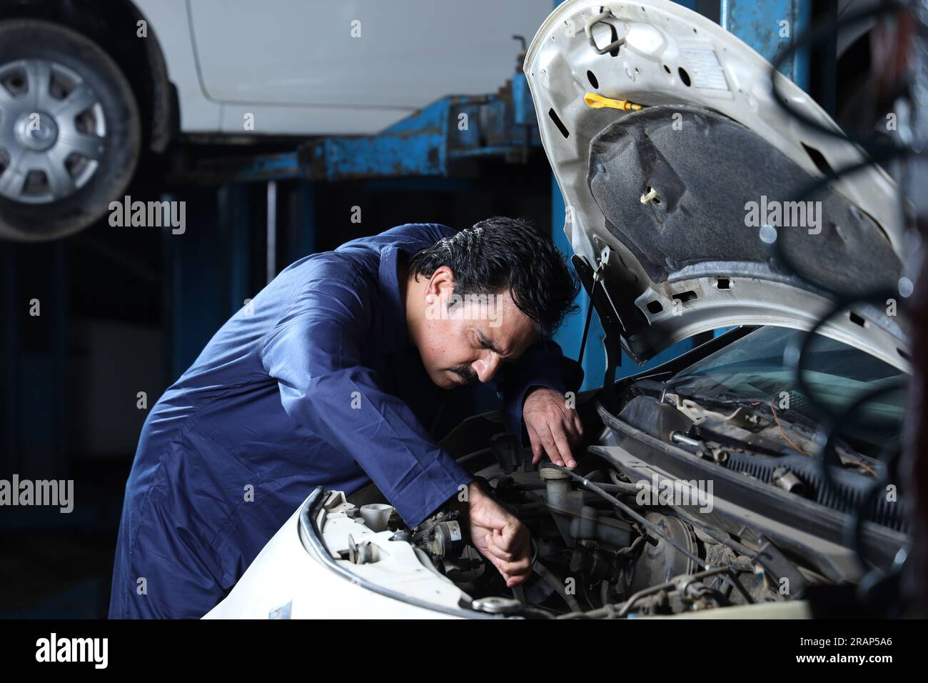 Close up portrait of hard working car mechanic standing in service station beside a car. Car Specialist is examining the engine. Stock Photo