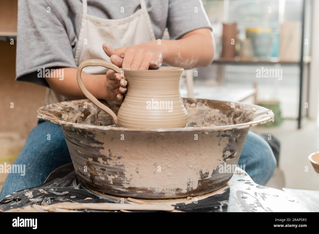 Cropped view of young female artisan in apron making clay jug while