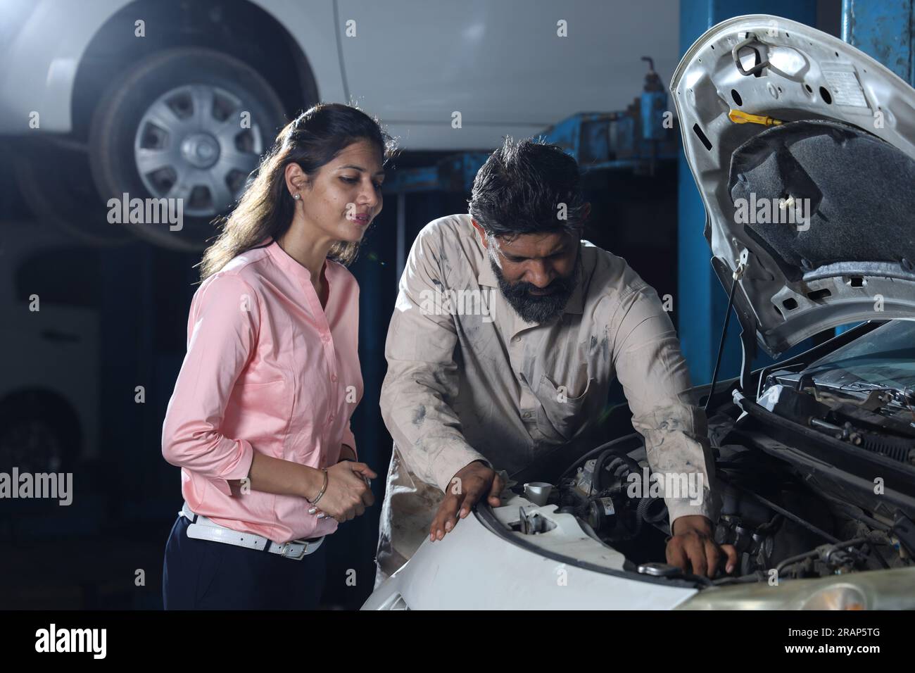 Close up portrait of bearded happy car mechanic standing in service station beside a customer. Car Specialist is examining the engine. Stock Photo
