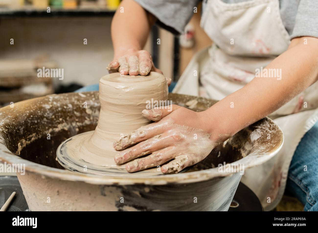 Cropped view of blurred female artisan in apron shaping wet clay and