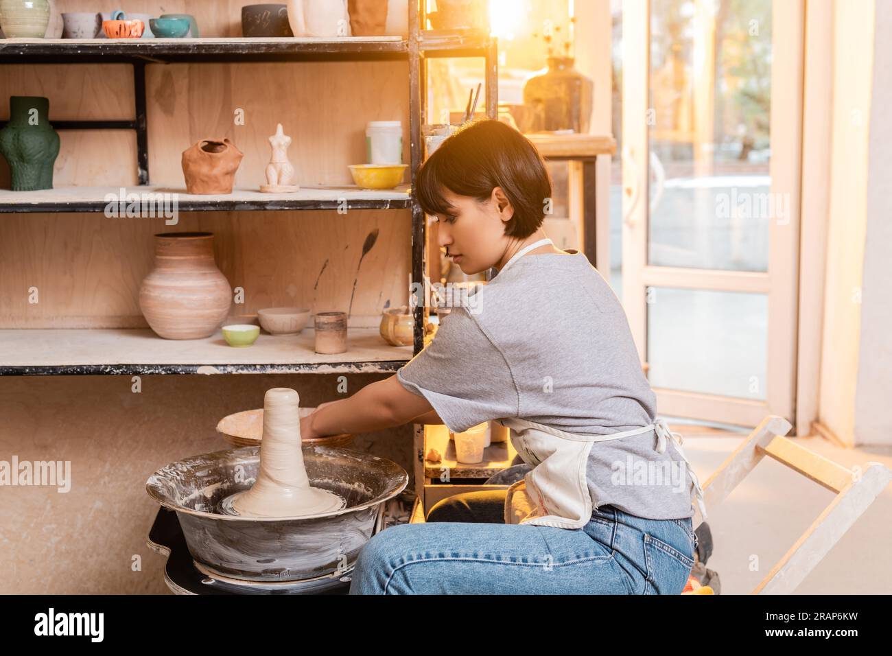 Side view of young asian artisan in apron working with wet