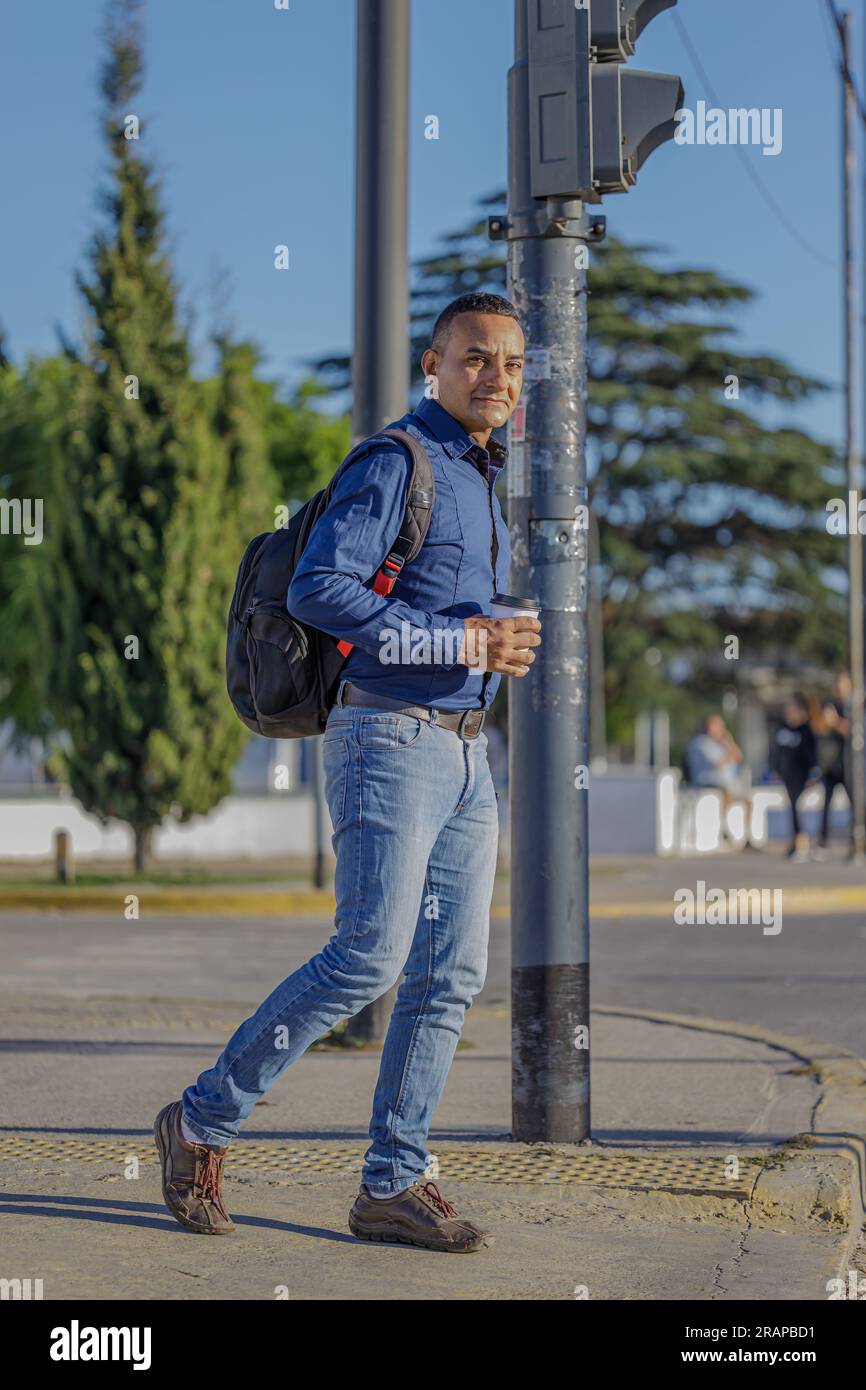 Young latin man with a disposable cup of coffee in his hand crossing the street in a city. Stock Photo