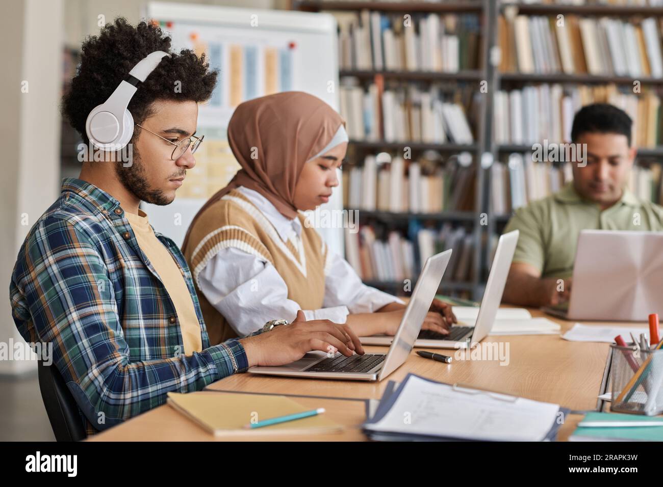 Group of foreign students using computers in their study while sitting at table in the library Stock Photo