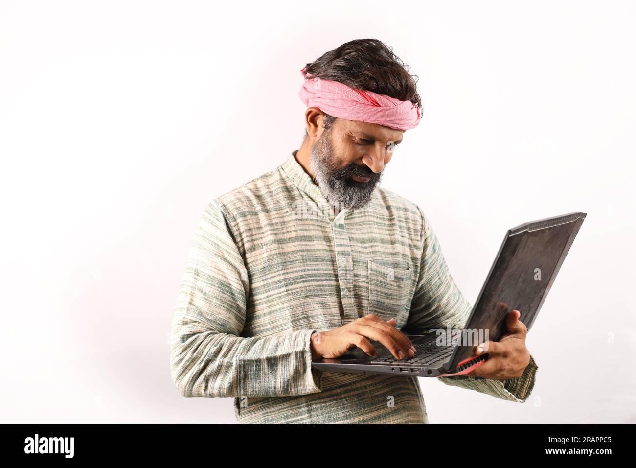 Portrait of an happy Indian bearded farmer man in rural India concept. White background cheerful confident farmer holding laptop and using technology. Stock Photo