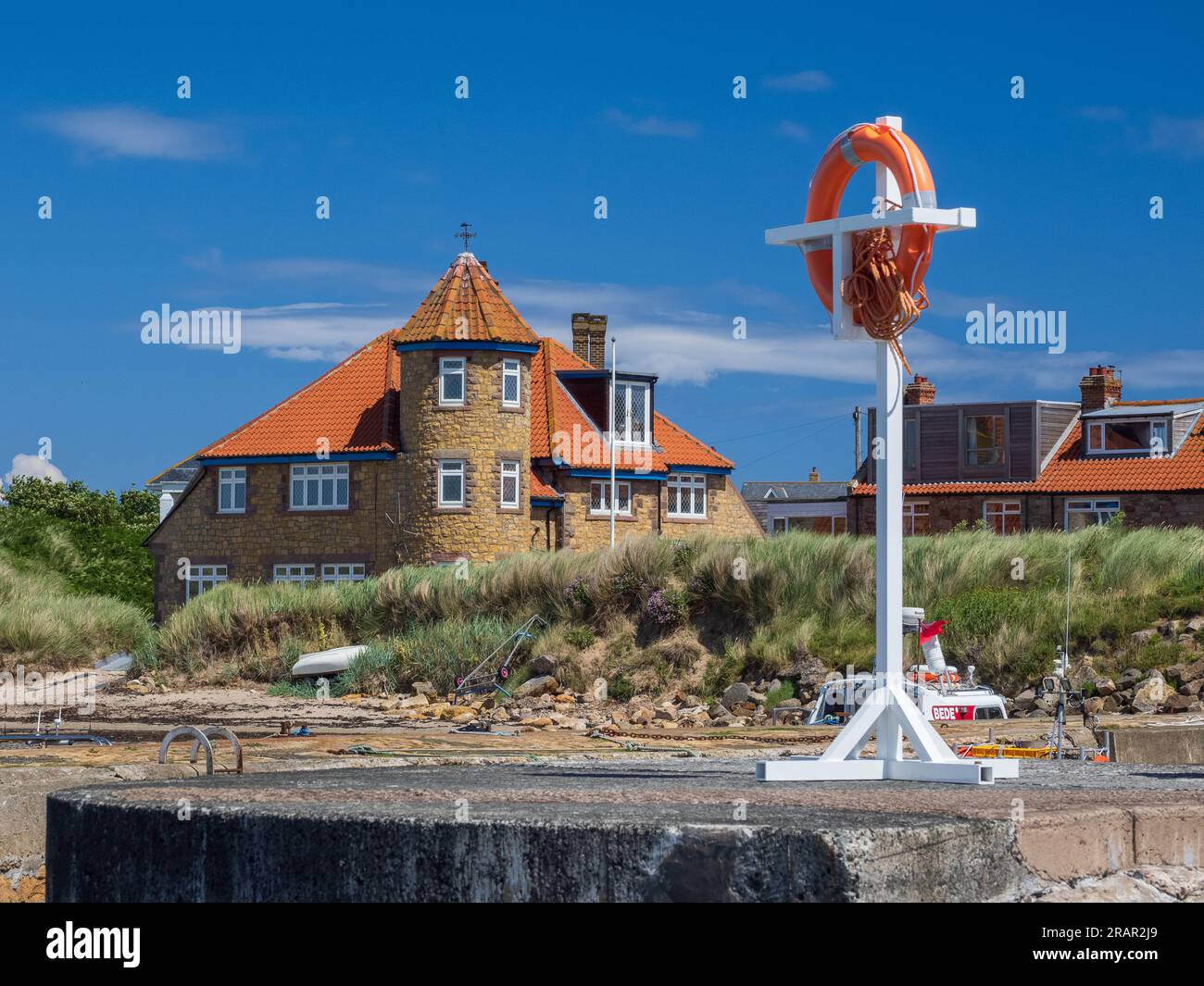 A sunny day at Beadnell Bay Northumberland UK, with a lifebelt in the foreground and Beach Court behind. Stock Photo