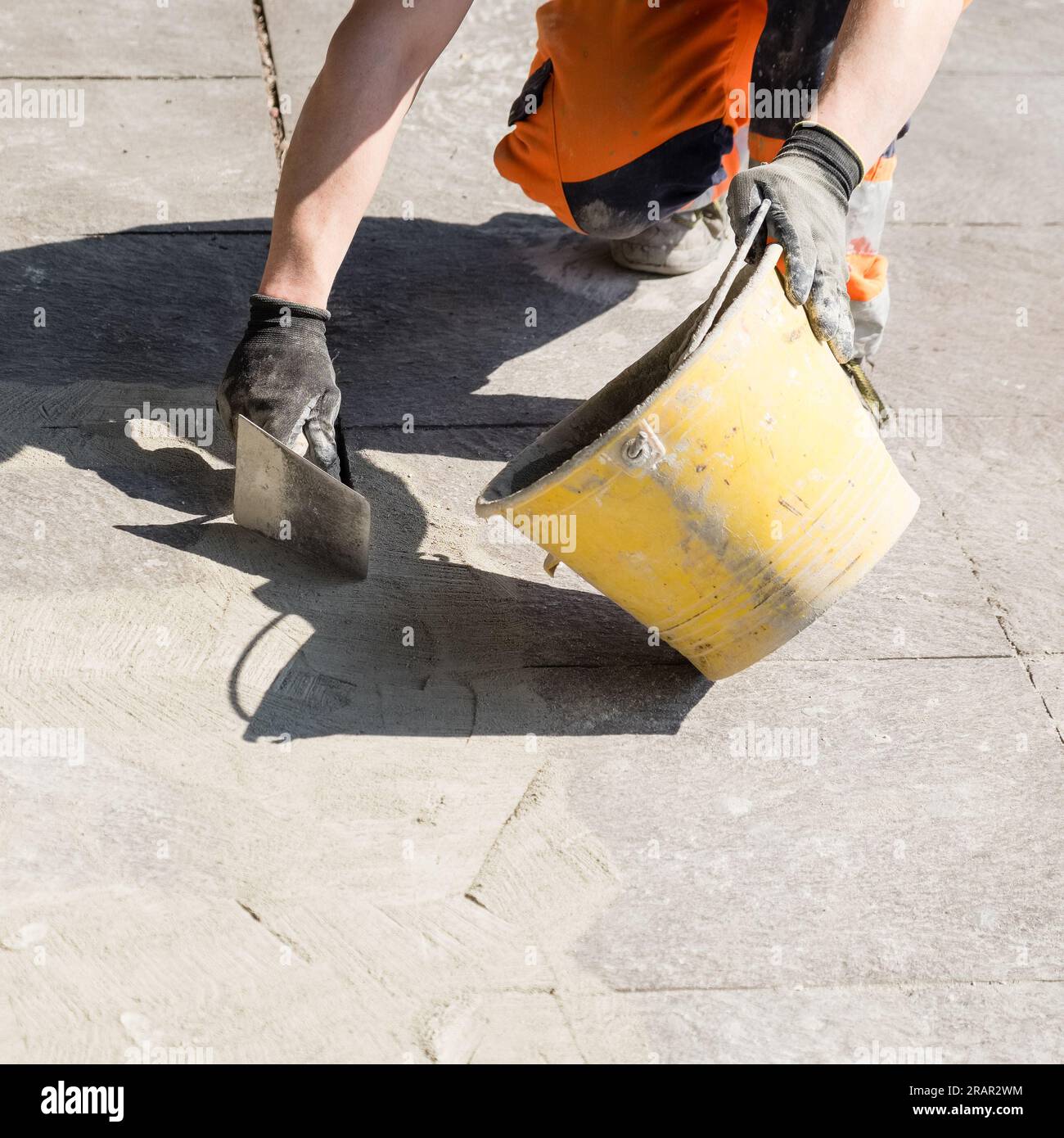 Real life scene, worker with trowel and bucket working on a pedestrian pavement. Stock Photo