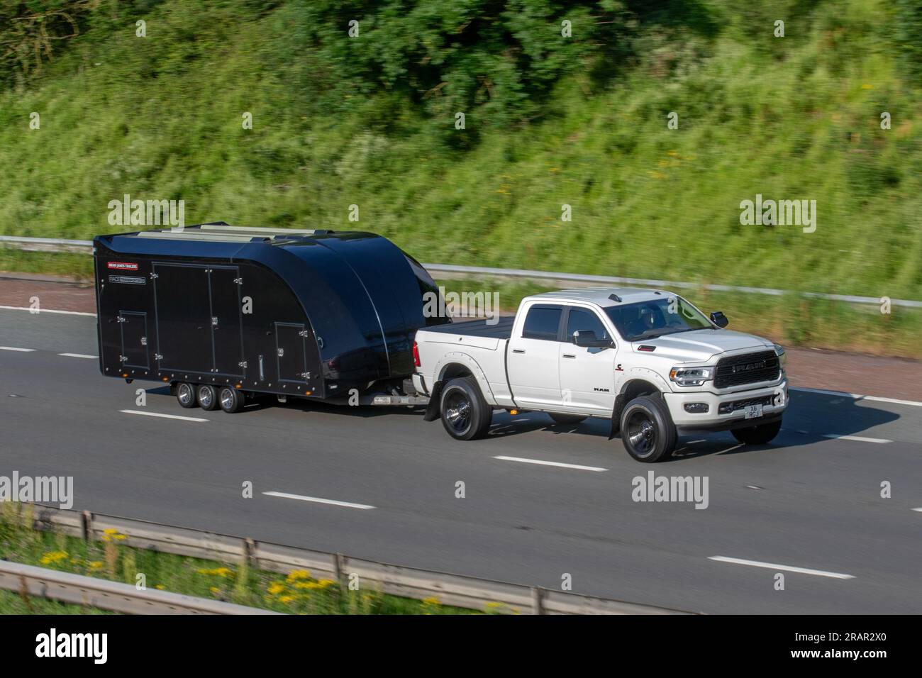 Brian James Race Transporter 6 - Enclosed Black car trailer, tri-axle car trailer towed by 2019 DODGE RAM Usa travelling at speed on the M6 motorway in Greater Manchester, UK Stock Photo