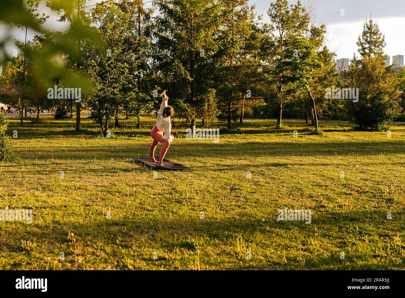 Remote side view of unrecognizable sporty young woman in sportwear doing Extended Side Angle pose during yoga class on evening in nature. Stock Photo