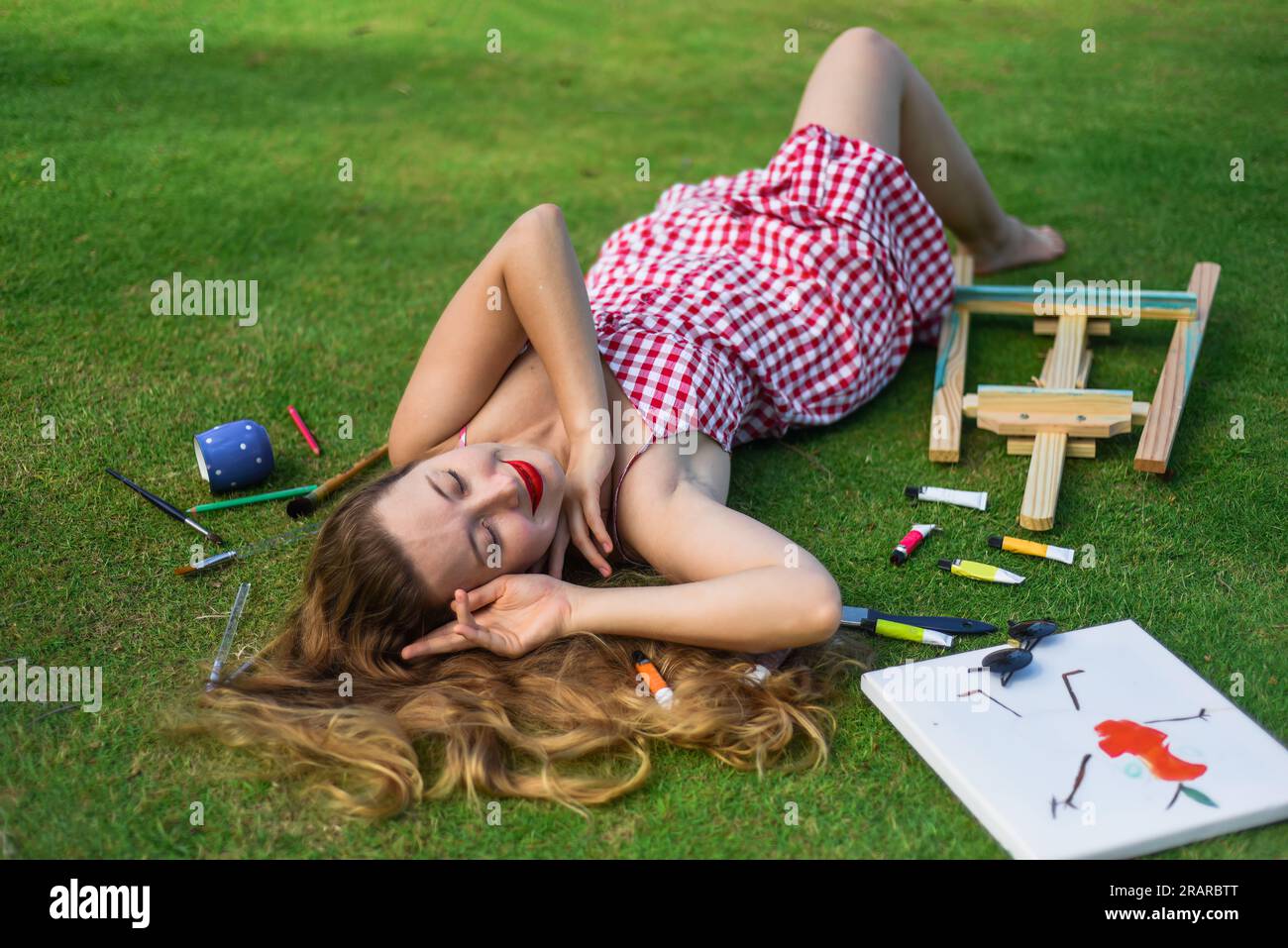 Beautiful woman artist and illustrator laying on the lawn with dropped easel, drawings, pencils Stock Photo