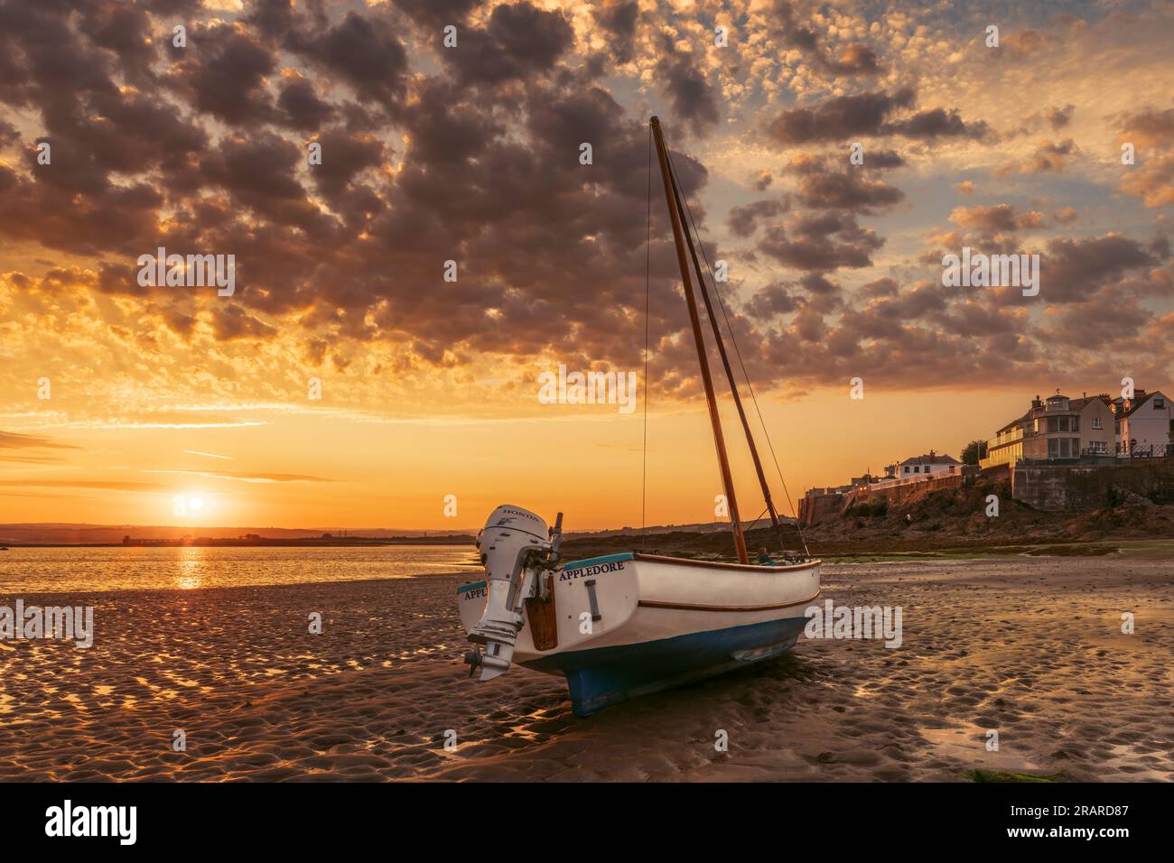 The sun crests the horizon on a late June sunrise, as the tide creeps towards one of the small boats that line the River Torridge estuary at Appledore Stock Photo