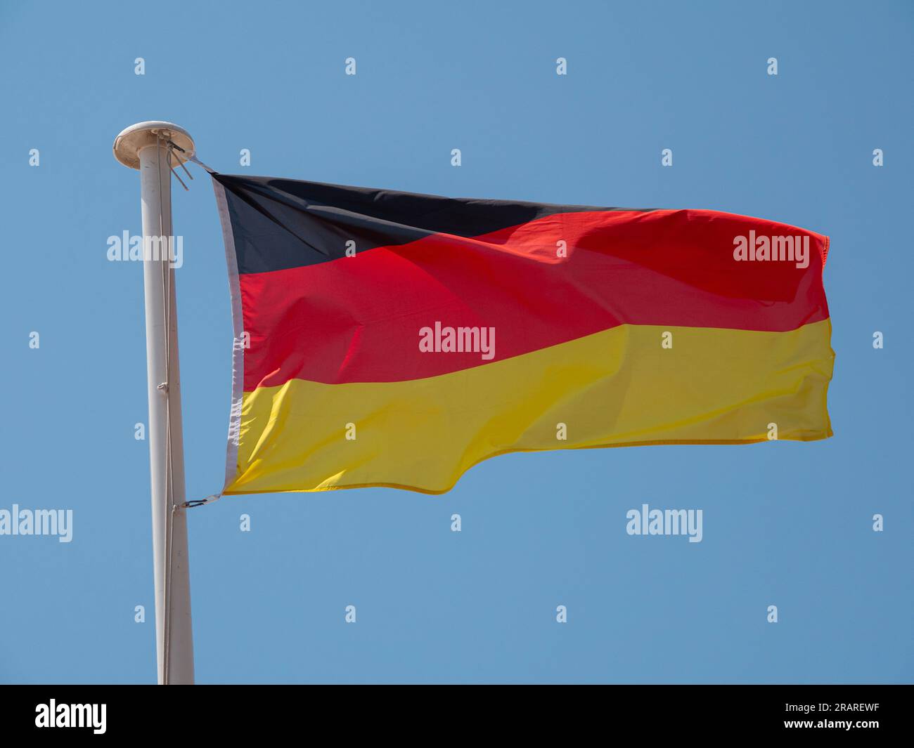 Germany the German national flag waving in the wind on a flagpole with blue sky background. Stock Photo