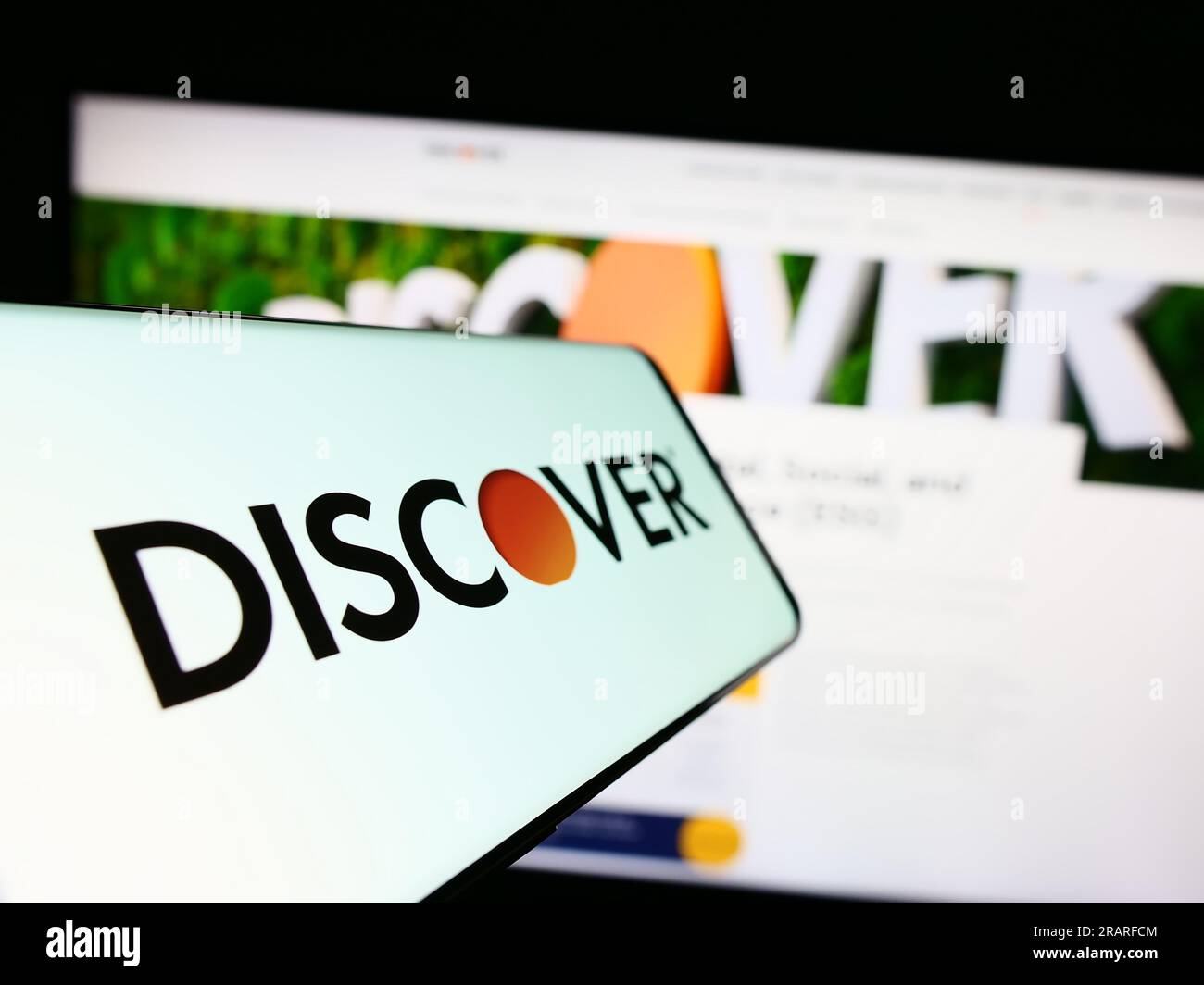 Mobile phone with logo of American company Discover Financial Services on screen in front of website. Focus on center-left of phone display. Stock Photo