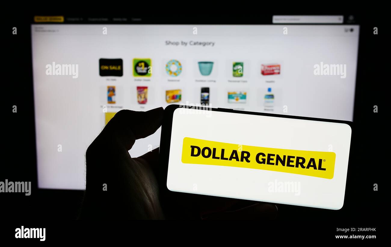 Person holding cellphone with logo of American retail company Dollar General Corporation on screen in front of webpage. Focus on phone display. Stock Photo